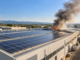 Incendio ai pannelli fotovoltaici della Salpa-Rolli a Roseto: nessun ferito, cause da accertare Illustrazione IA di pannelli fotovoltaici su un capannone industriale con fumo in lontananza.